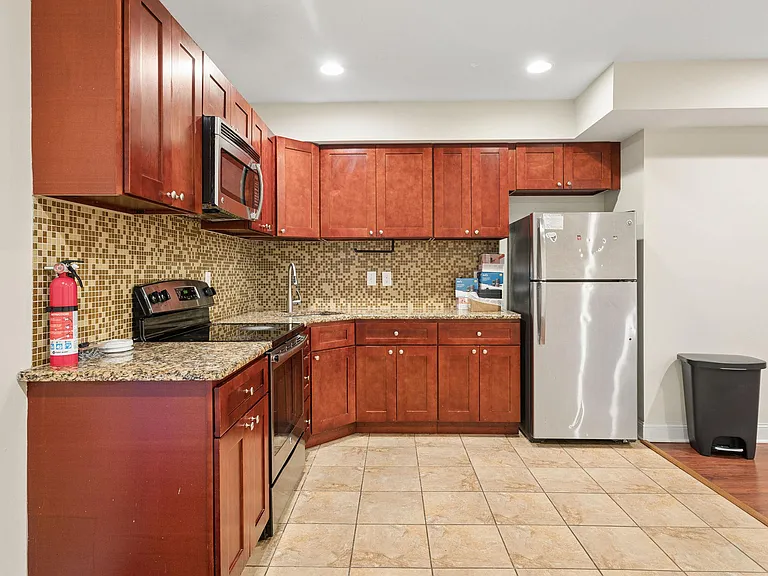 Efficient L-shaped kitchen with ample wood cabinetry, mosaic tile backsplash, granite-look counters, and stainless appliances