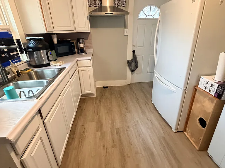 Galley-style kitchen with ample white cabinetry, double-basin sink, and full-size refrigerator plus vent hood.