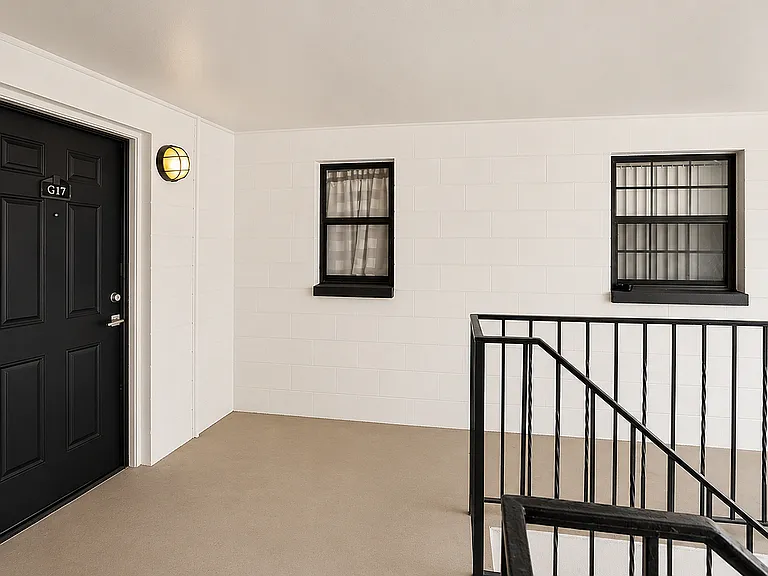 Modern apartment entrance featuring a sleek black door labeled G17, with stylish windows and elegant railing in a clean white hallway.