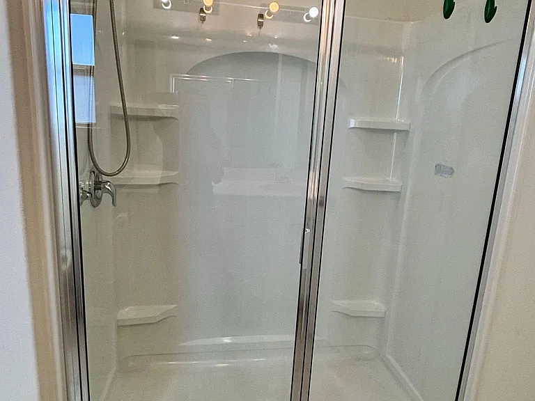 Spacious walk-in shower with sliding glass doors, built-in shelving, and easy-care tile flooring.