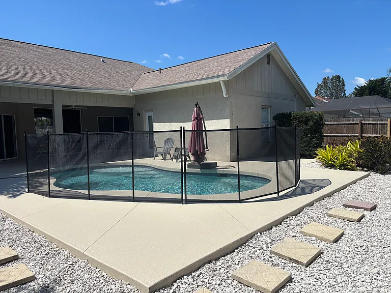 Outdoor pool area with baby gate fence around pool. Completely fenced yard with small grass area. Double gate at back of property. She'll rock along outer edge of pool deck