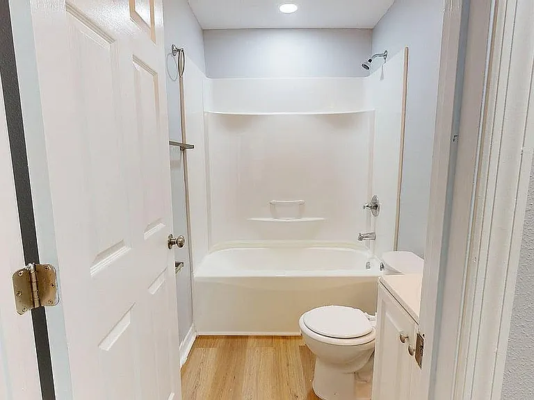 Bright and modern bathroom featuring a sleek bathtub, elegant white fixtures, and stylish wooden flooring.
