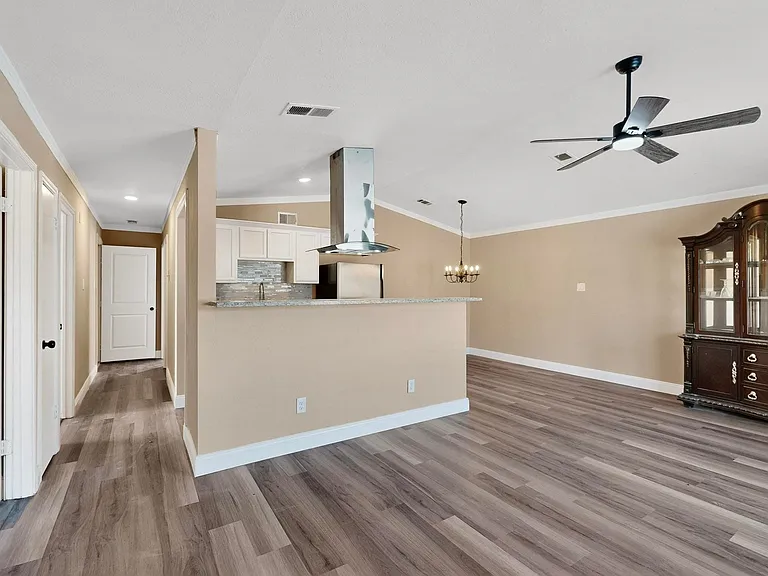 Kitchen featuring backsplash, island exhaust hood, crown molding, white cabinets, and wood finished floors