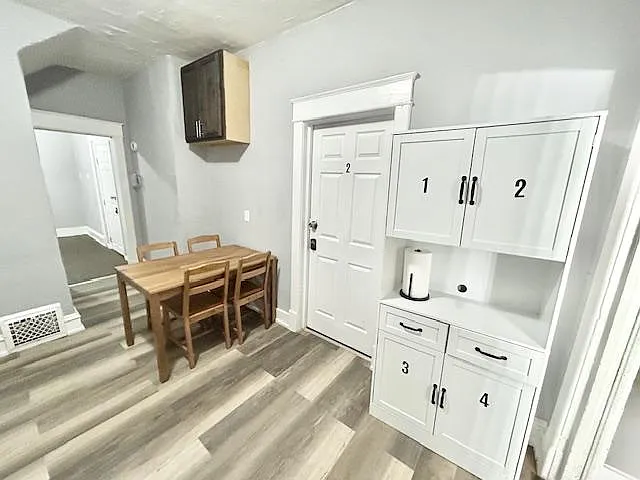 Dining area with a table for four, durable plank flooring, and built-in cabinet storage near the entry.
