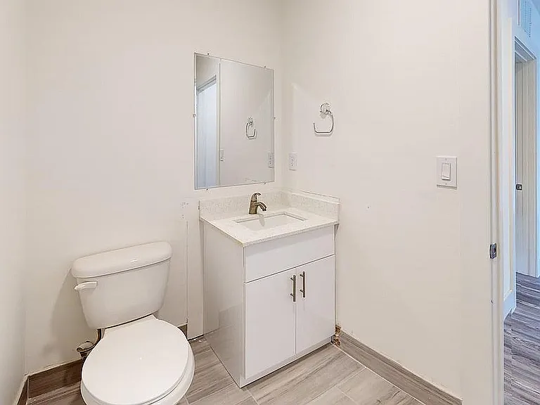 Bright and modern bathroom with sleek fixtures, pristine vanity, and wood-style flooring, ideal for a stylish apartment living.