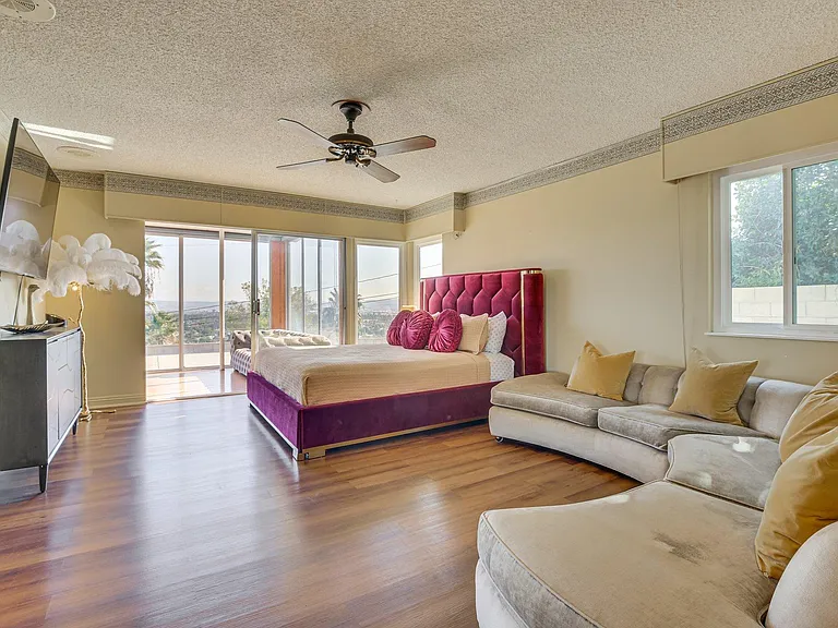 Spacious bedroom with a sitting area, wood-style floors, ceiling fan, and sliding doors leading to a private balcony.
