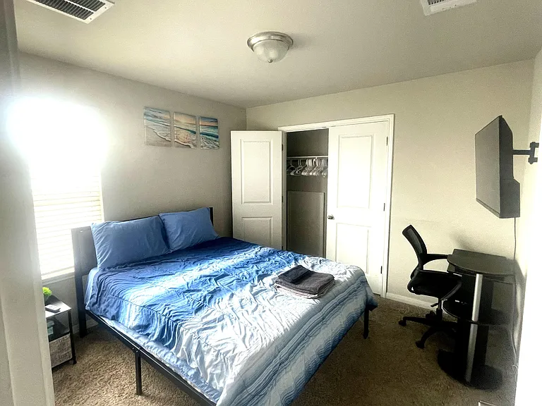 Furnished bedroom with a full-size bed, window with blinds, open closet storage, and a dedicated desk/workspace.