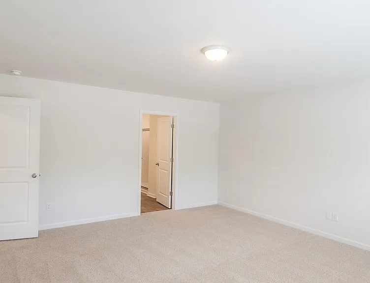 Expansive primary bedroom with soft neutral carpet, high ceilings, and recessed lighting. Generous proportions easily accommodate a king-size bed and sitting area. Multiple doorways lead to a walk-in closet and en-suite bathroom.