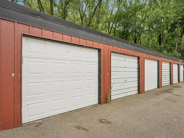 Left-most in the photo, extra-deep single garage with storage shelving or weather-safe items.