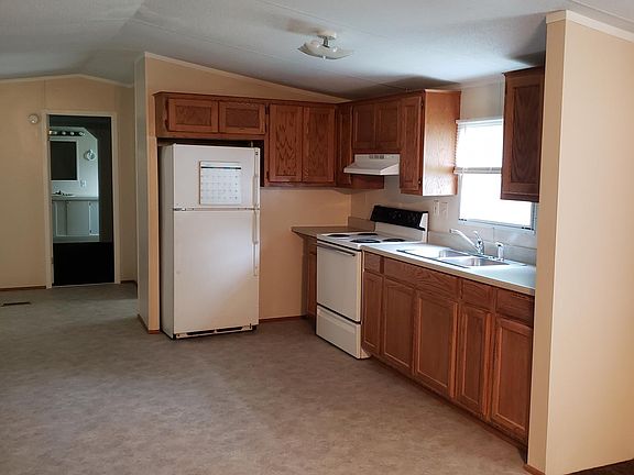 Standing in living room looking at kitchen cabinets, stove and refrigerator.