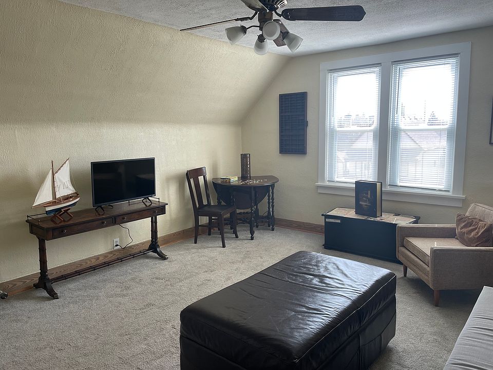 Carpeted living room with west facing windows and ceiling fan.