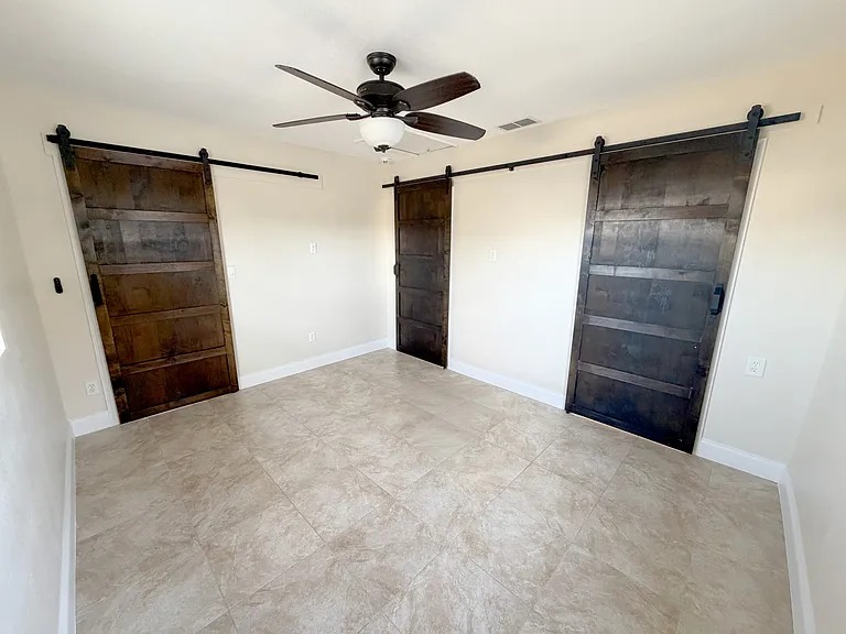 The master bedroom offers abundant natural light, a ceiling fan for comfort, and modern barn doors. (Angle 2)