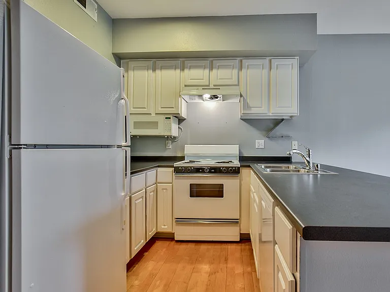 Kitchen featuring wood-finish flooring, white cabinetry with dark countertops, and a stainless steel sink with a chrome faucet