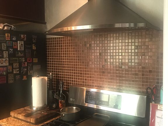 Beautiful stainless steel chef stove with six burners, and beautiful stainless steel vent fan and hood. Note granite countertop, and glass tiled backsplash.