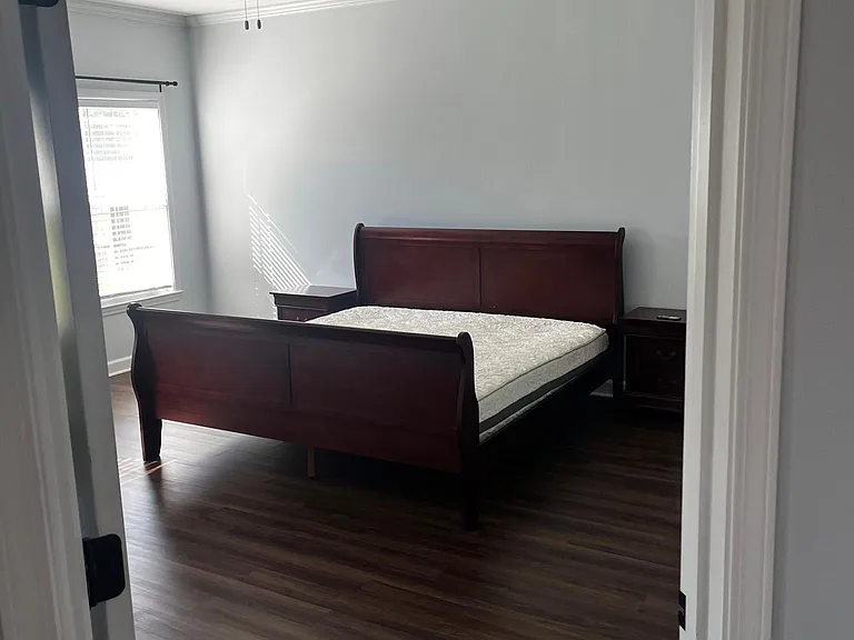 Spacious primary bedroom with tray ceiling, ceiling fan, dark flooring, and included bedframe and end tables.