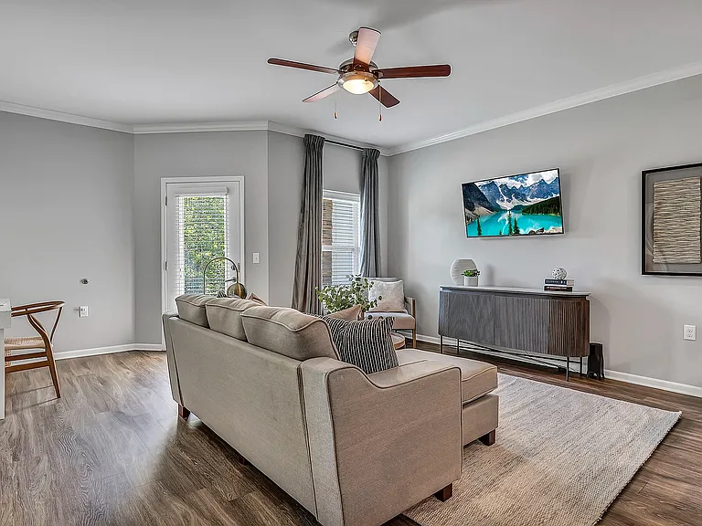 Enjoy the practical peace of a comfortable, grounded living area, with plenty of natural light, wood-style flooring, a ceiling fan, and access to your private patio or balcony.