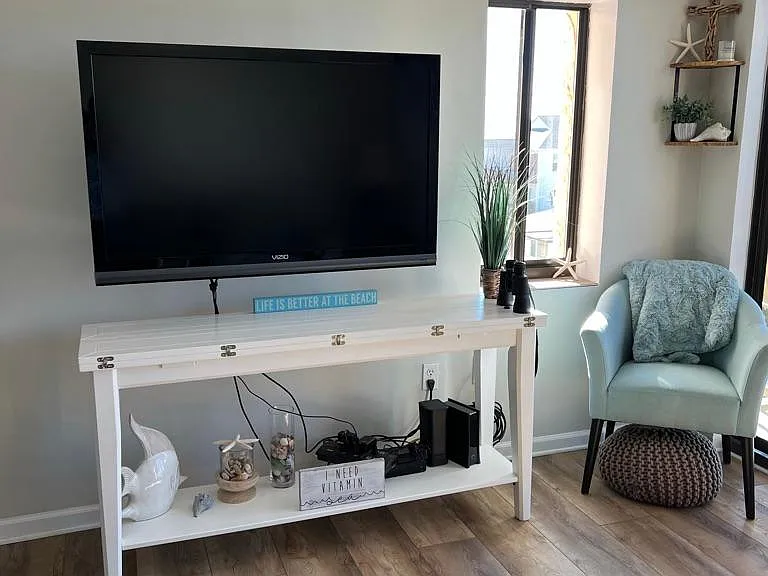 TV in living area with side window that has a view of the ocean.