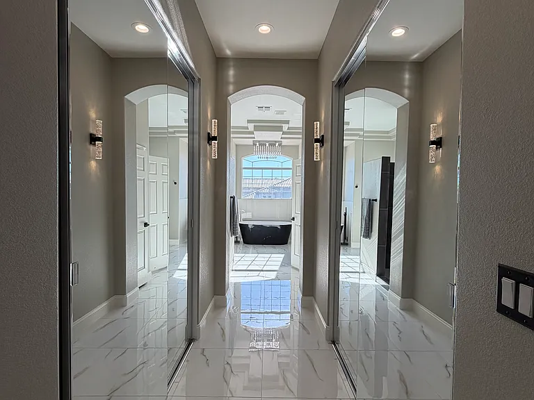 Primary suite hallway with dual mirrored closets on both sides, leading to the spa-inspired ensuite bathroom