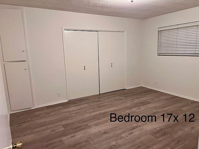 Bedroom with plank flooring, large closets, air conditioning unit and faux wood blinds