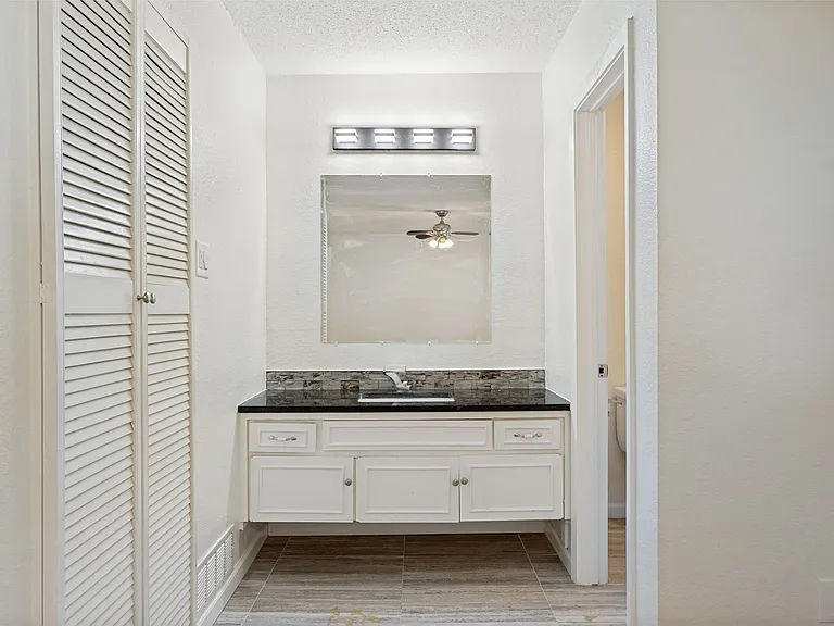 White vanity with dark countertop and mosaic tile backsplash, featuring a rectangular mirror with overhead light fixture