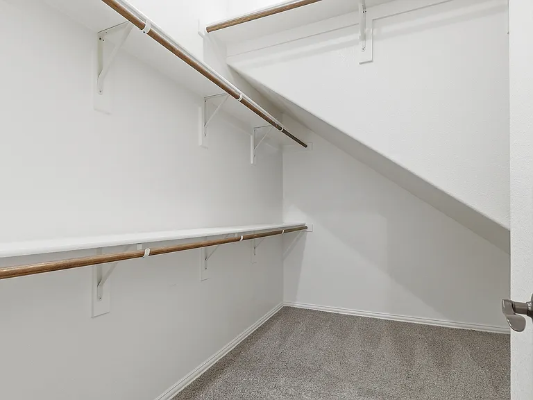 Walk-in closet with multiple white shelving units, wood-finish hanging rods, gray carpet, and white baseboards