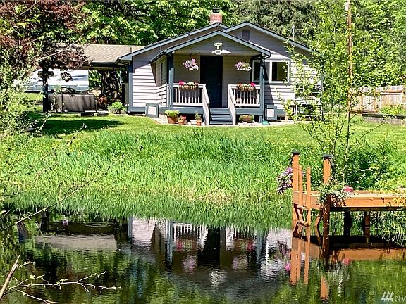 looking from across the pond. Freshly painted trim, covered patio+front porch, garden space to the right.