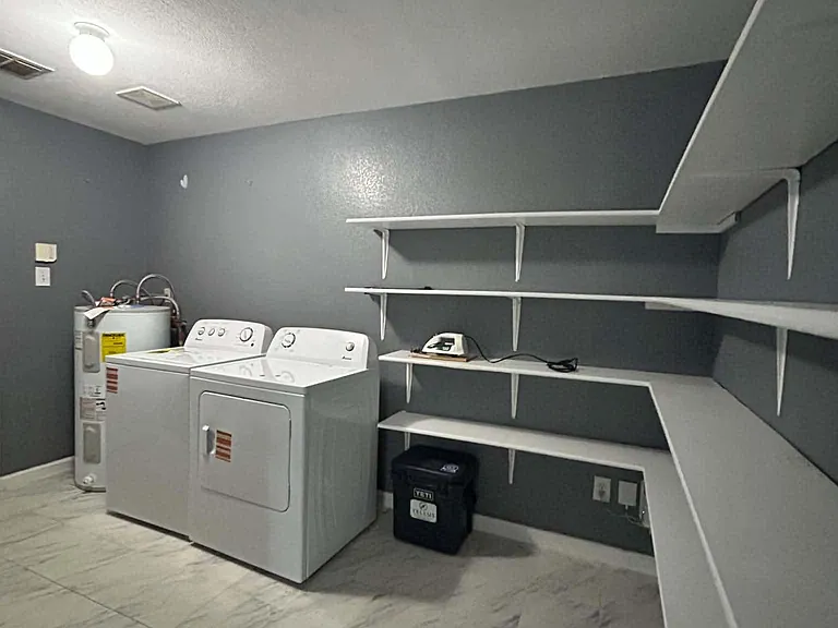 Dedicated laundry room with washer/dryer, durable tile flooring, and extensive built-in shelving for storage.