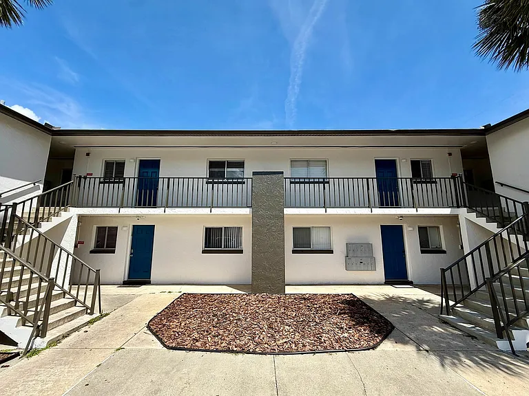 Charming modern apartment complex with vibrant blue doors, spacious balconies, and well-maintained landscaping under a clear blue sky.