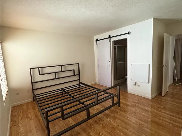 Primary bedroom with barn door for the bathroom. Bedroom window faces North. Bed frame size is California King but not included with the rental.