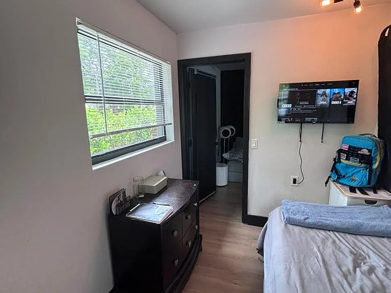 Private bedroom with a large window, wood-style flooring, and space for a dresser plus wall-mounted TV.