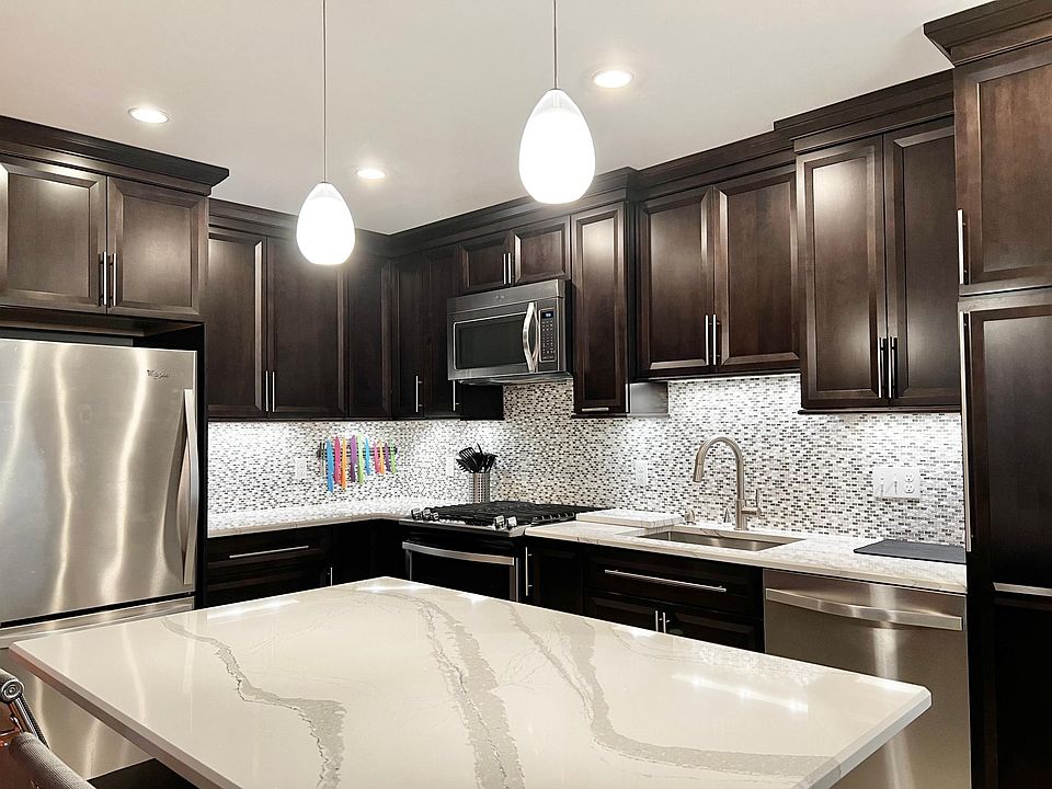 Beautifully remodeled kitchen with center island, custom cabinetry, quartz countertops, gas range, and stainless steel appliances
