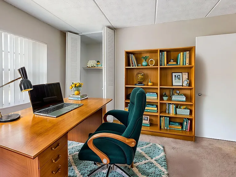 Bright and inviting home office space with a sleek wooden desk, modern lamp, and comfortable green chair, ideal for productivity. Large window provides natural light, with a stylish bookshelf enhancing the cozy atmosphere.