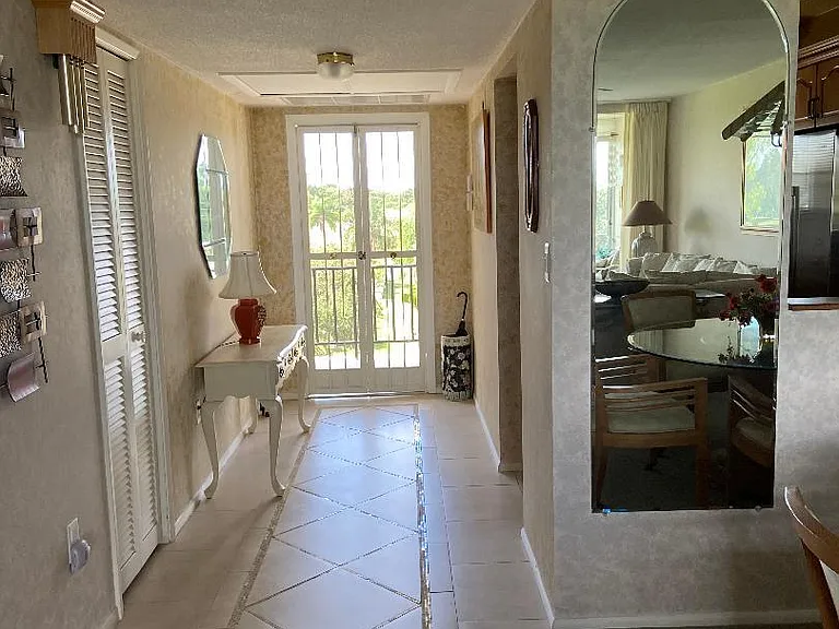View from dining room through entrance hall toward open front door onto exterior walkway. Mirror on wall reflects view toward lanai.