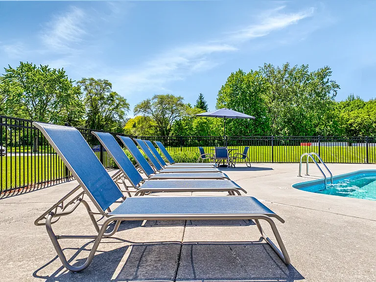A row of sun lounge chairs are set up by the pool.