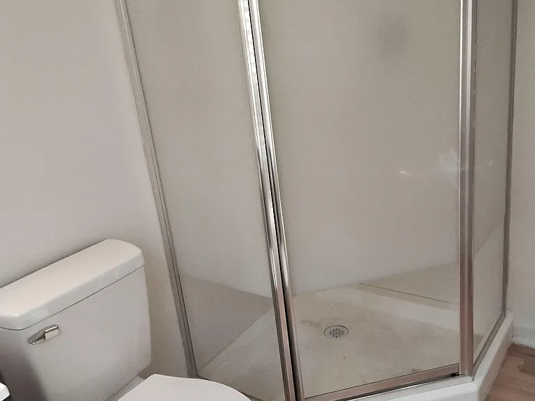 Bathroom features a corner glass-enclosed shower and a standard toilet with easy-clean flooring for everyday use.