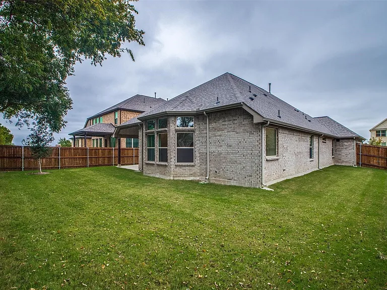 Expansive fenced yard featuring a brick exterior with multiple windows and a covered patio