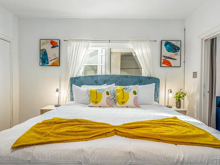 Bathed in natural light from the large window, the room is accented with sleek nightstands, modern lamps, and tranquil artwork.