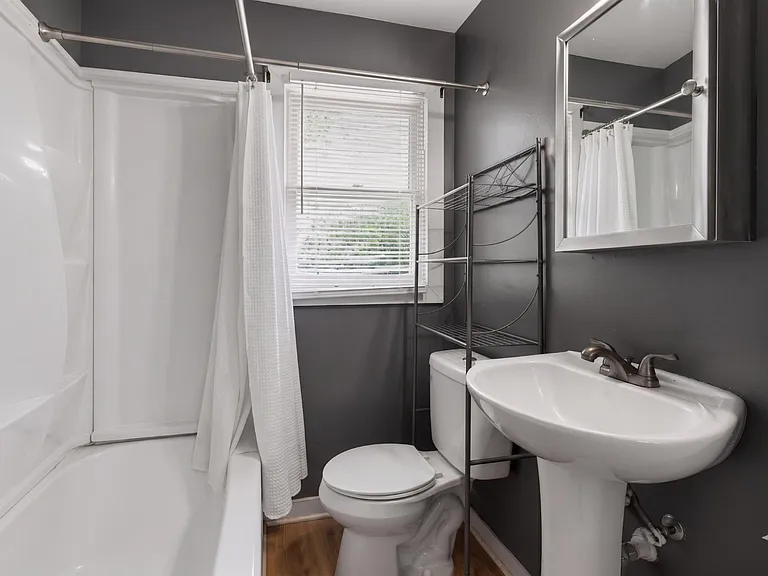 Full bathroom with tub/shower combo, pedestal sink, and a window plus over-toilet shelving for extra storage.