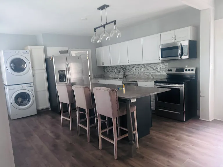Kitchen with large island, stackable washer and dryer, double door ice maker refrigerator, flat glass top stove with oven, microwave and dishwasher.