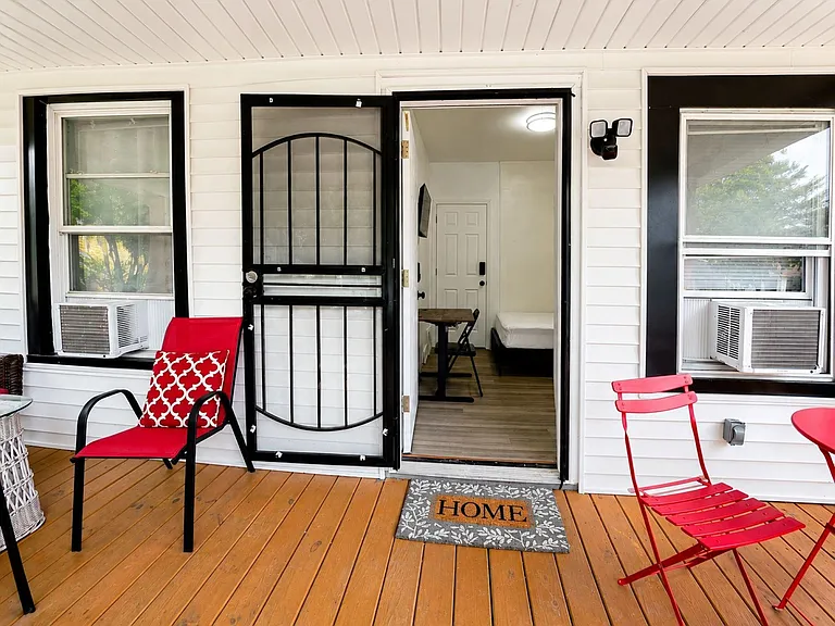Inviting covered front porch with seating, a secure storm door entry, and convenient window A/C units for comfort.