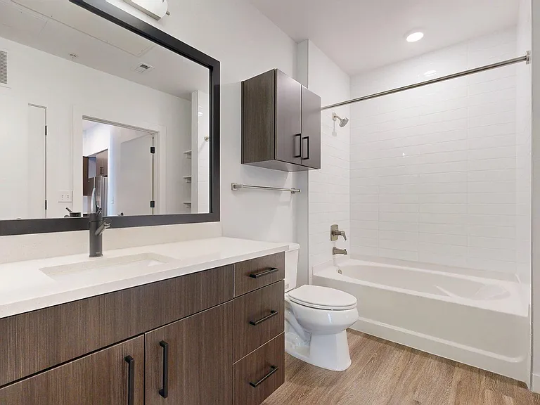 A modern bathroom with a dark wood vanity, white countertop, and a shower/tub combo.