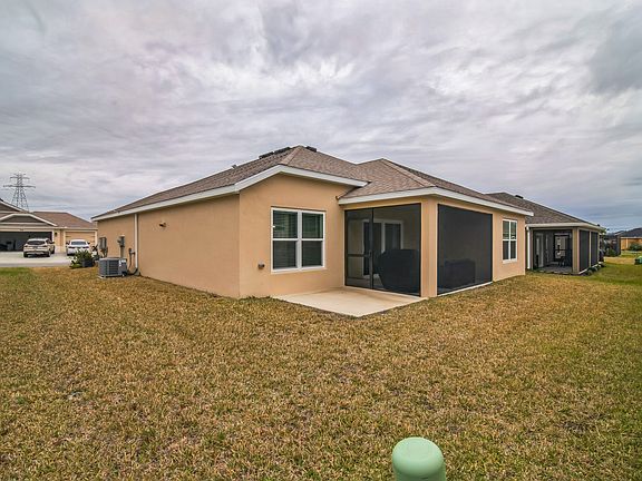 Backyard View of the House with Side Yard, Dining Room Window, Concrete Patio, and Enclosed Birdcage/Lanai.