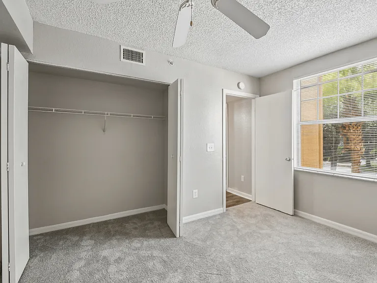 Carpeted bedroom with large closet, window, and neutral color palette in a 3-bedroom, 2-bath apartment at Gregory Cove in Jacksonville, FL.
