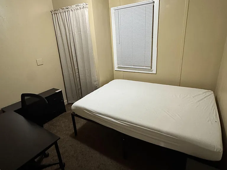 Private bedroom with a window, overhead lighting, and space for a bed and small work setup.