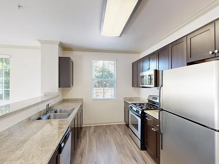Apartment kitchen with stainless steel appliances, quartz countertops, and wood-style flooring.