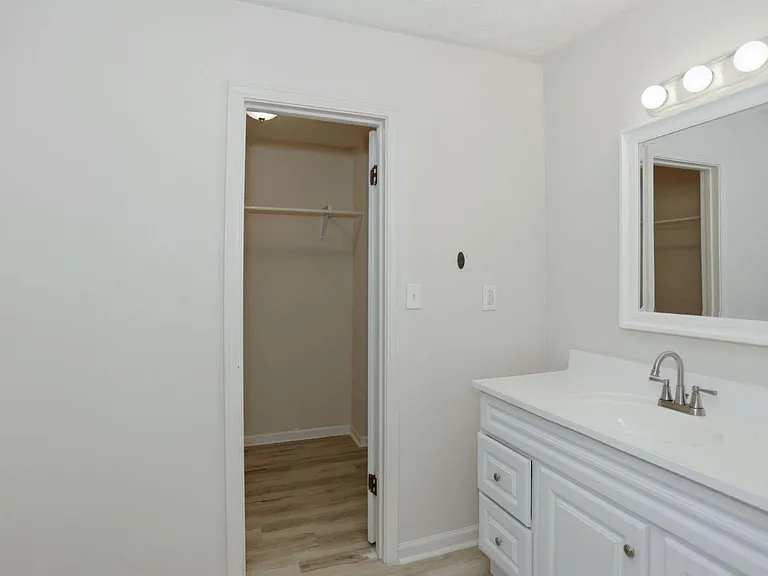 Updated bathroom vanity with ample storage, large mirror and overhead lighting, plus a nearby closet for extra organization.