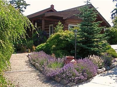 Welcoming garden path. This single level log home stretches out beyond the gardens.