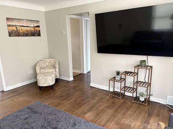 Living room with hardwood floors, wall-mounted TV, and an open pass-through to the hallway for easy flow.