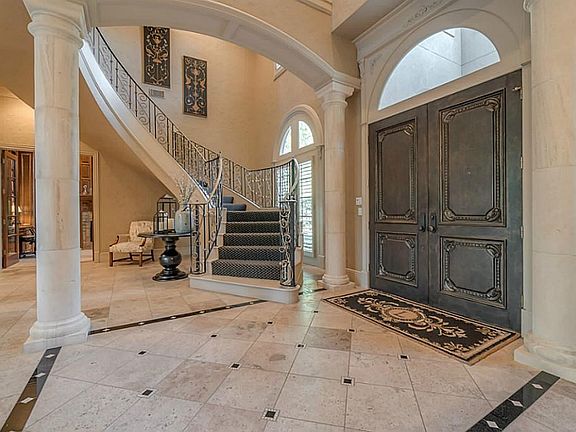 Sweeping staircase with stone floors and dramatic columns throughout foyer area.