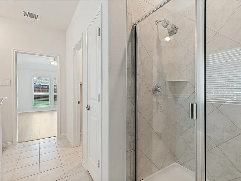 Glass-enclosed shower featuring diagonal tile work, integrated shelving, and a chrome shower head